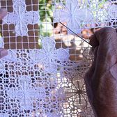 Hands working a needle through white openwork lace