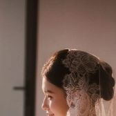 Bride in a long ivory lace veil seated in soft window light