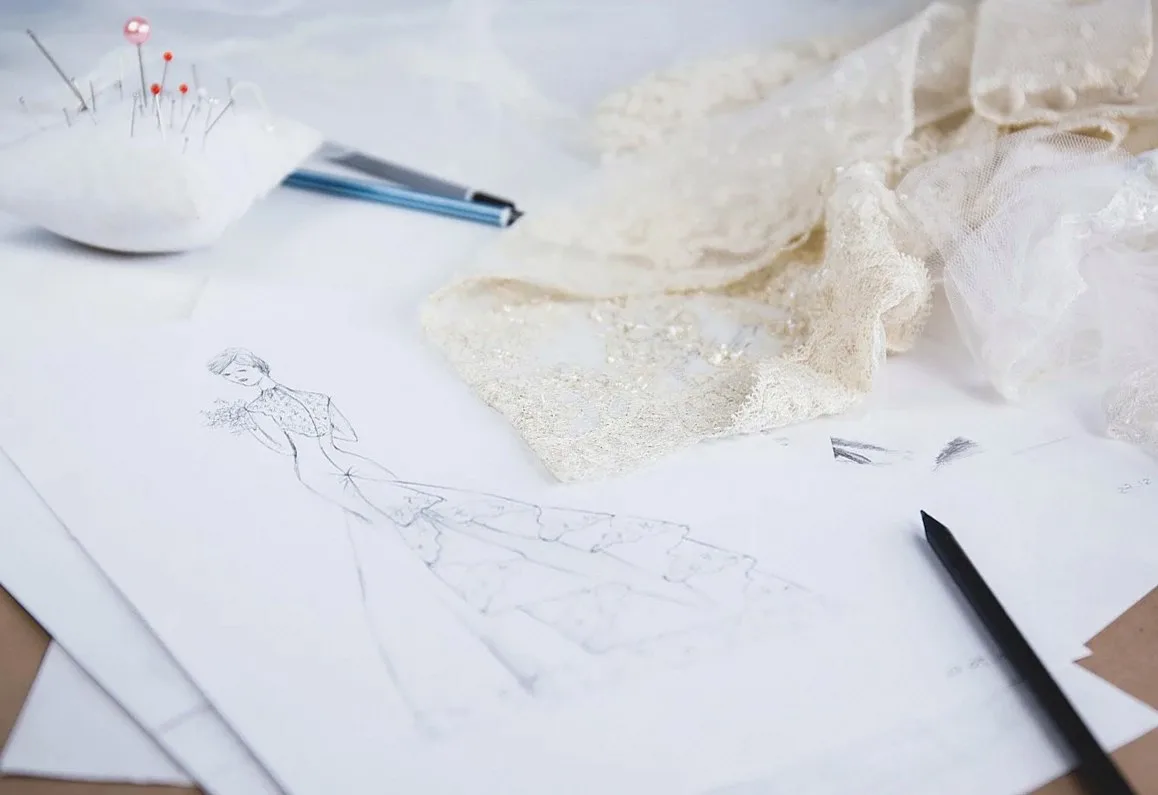 Pattern sketches and cream lace laid out on a worktable