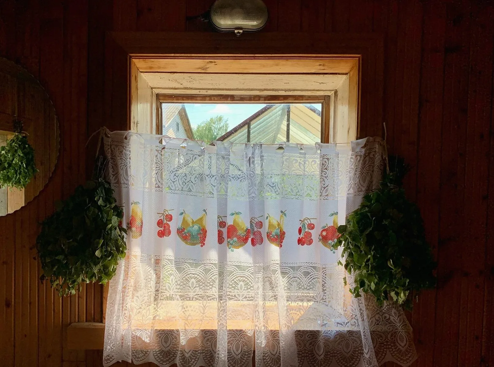 Lace curtains hanging in a wooden window frame with plants on either side