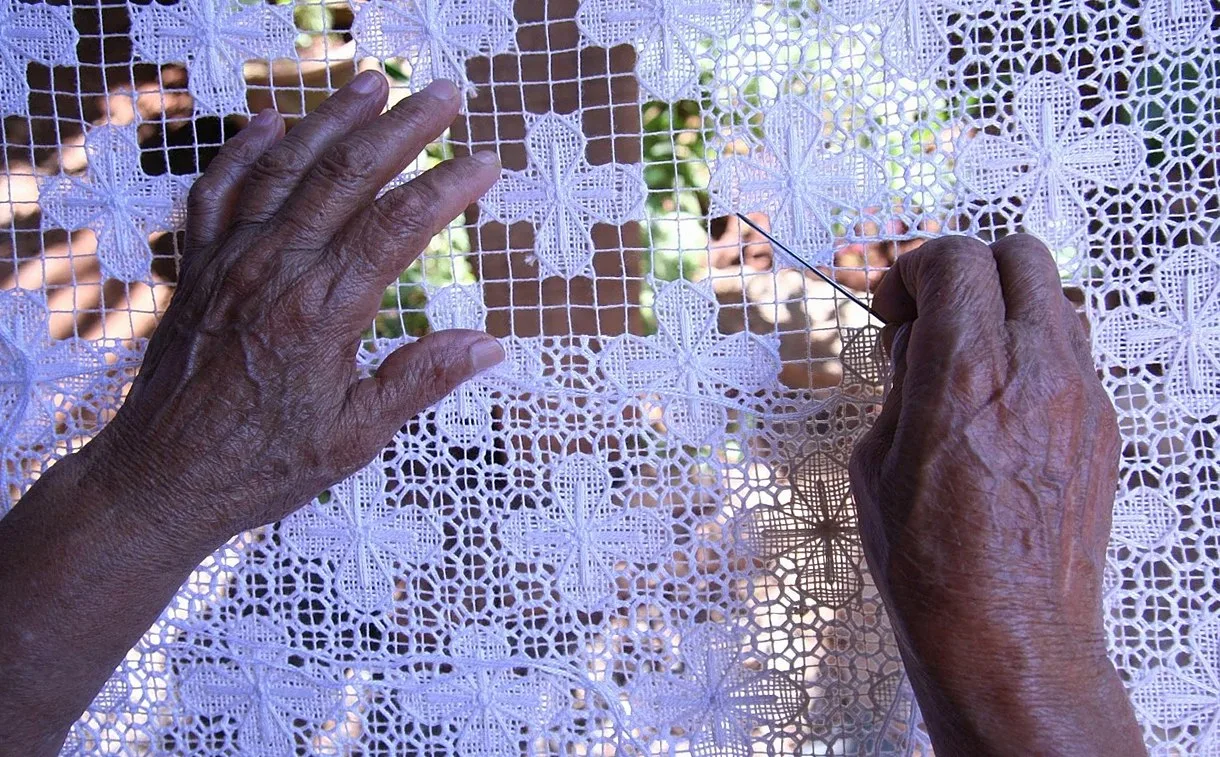 Hands working a needle through white openwork lace