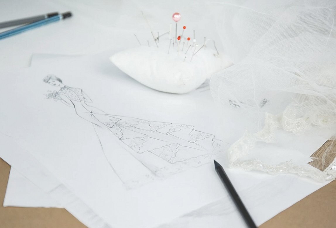 Pattern sketches, a pincushion and cream lace trim on a worktable