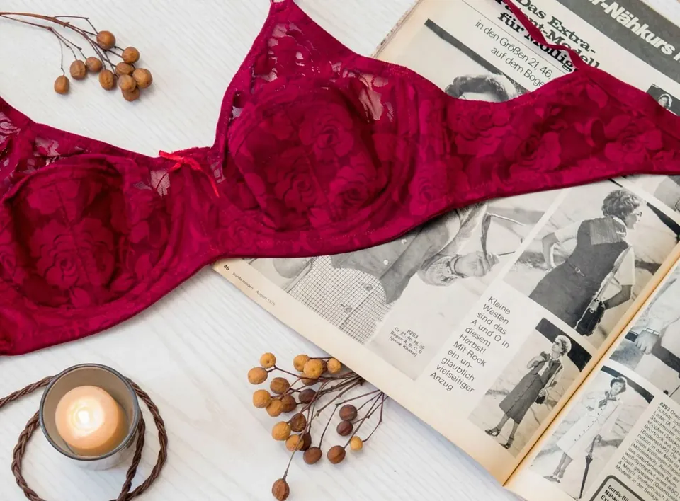 Red lace bra laid flat on a white table beside a candle and vintage magazine pages